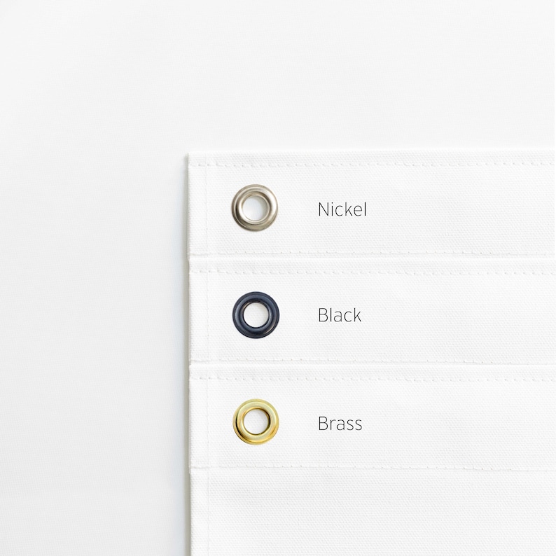 May include: Close-up of three grommets in different finishes: nickel, black, and brass. The grommets are on a white fabric background.