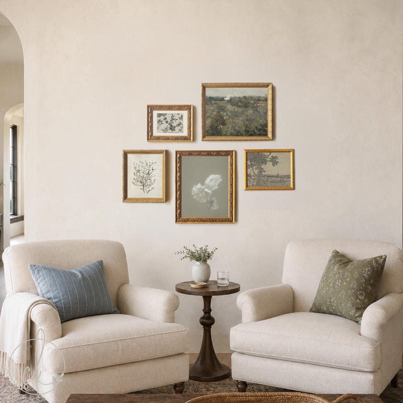May include: Two beige upholstered armchairs with a blue striped cushion and a green floral cushion, separated by a dark wood pedestal table with a small white vase. Five framed art prints with gold frames are arranged on the wall above them.