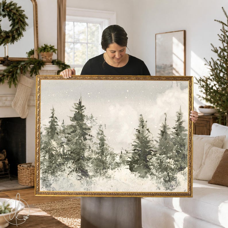 May include: A rectangular landscape painting in a gold ornate frame depicting a winter forest scene with dark green pine trees, a snow-covered ground, and white specks representing falling snow against a soft, muted beige and grey sky.