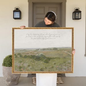 May include: A framed landscape print with a gold ornate frame. The artwork depicts a field with green and brown tones under a cloudy sky. Text in the upper portion reads, "May the God of hope fill you..." A decorative piece for home decor.