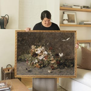 May include: A framed floral still life painting with a gold ornate frame. The artwork features a bouquet of white, yellow, and burgundy flowers with butterflies. The background is a dark, textured surface.