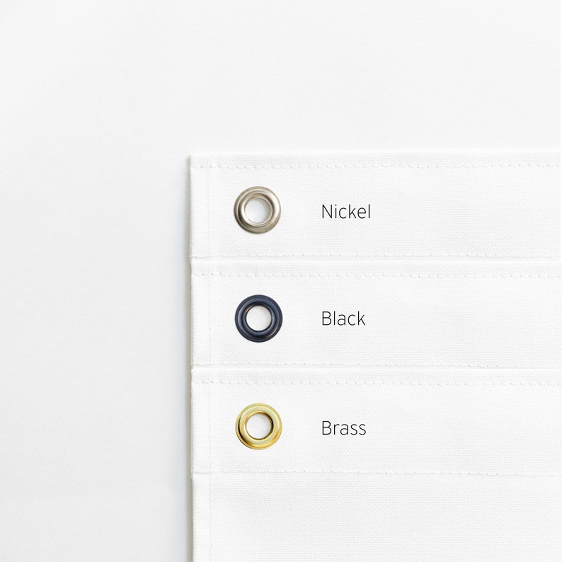 May include: Close-up of three grommets in different finishes: nickel, black, and brass. The grommets are on a white fabric background.