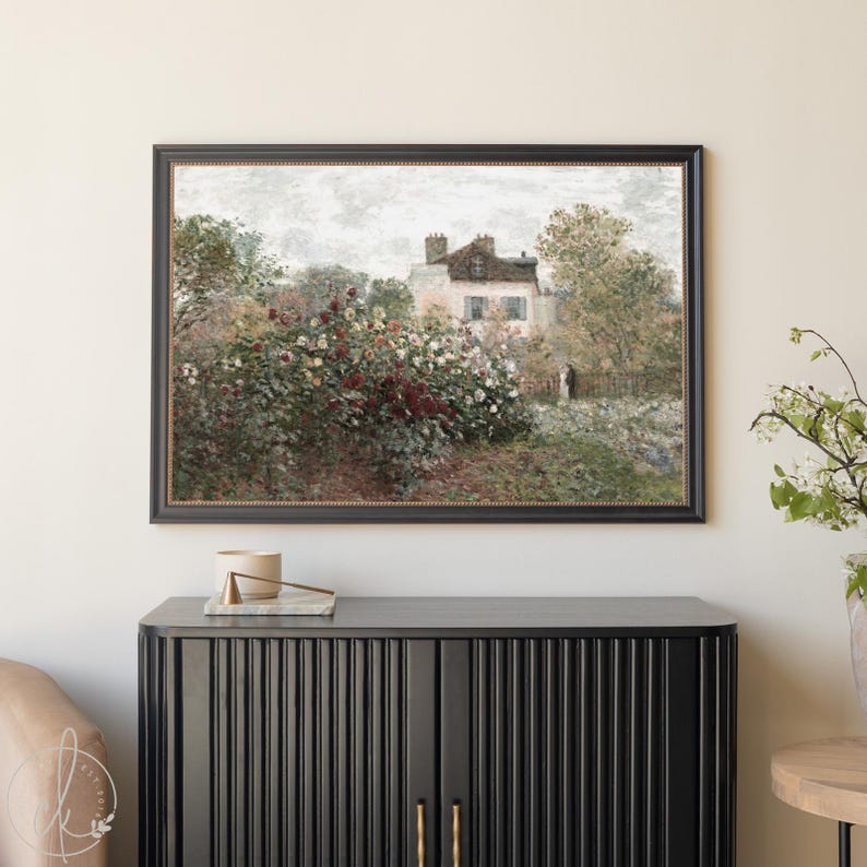 May include: A framed art print depicting a house nestled amongst a garden of flowers and trees. The painting has a vintage style with a muted colour scheme of greens, browns, and whites. The frame is black with a decorative edge.