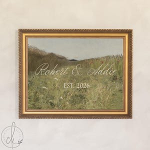 May include: A rectangular wall art piece in a decorative gold frame featuring a landscape painting of a grassy field with wildflowers. The text "Robert & Addie" is written in white script, with "EST. 2026" printed in white block letters below.