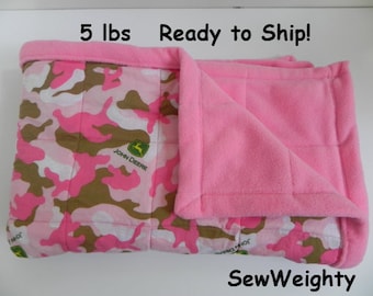 May include: A pink and brown camouflage patterned blanket with a pink fleece border. The blanket has a John Deere logo and is quilted. The blanket weighs 5 lbs.