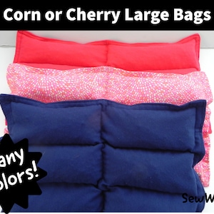 May include: Three large heat packs, one red, one pink with white polka dots, and one navy blue. The heat packs are stacked on top of each other. The text "Corn or Cherry Large Bags" is at the top of the image. The text "Many Colors!" is in a starburst shape at the bottom left of the image. The text "SewWeighty" is at the bottom right of the image.
