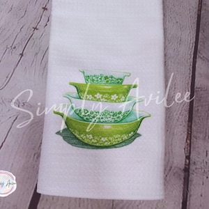 Puede incluir: Toalla de cocina blanca con un diseño de cuatro cuencos para mezclar verdes y blancos con estampado floral apilados. La toalla tiene el texto "Simply Avilee" y un logotipo. Los cuencos son de diferentes tamaños.