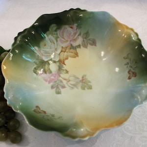 May include: A vintage porcelain bowl with a scalloped edge and a floral design featuring roses and leaves in shades of green, pink, and white.