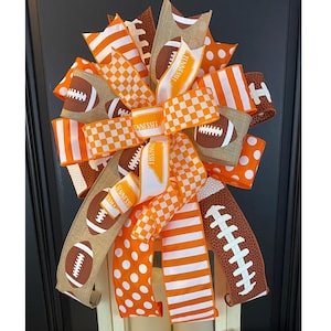 May include: A white lantern with a large orange and white bow on top. The bow is made of various ribbons with football designs and the word "Tennessee" on it.