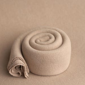 Pu&ograve; includere: Uno sfondo in tessuto beige arrotolato per la fotografia di neonati. Il tessuto &egrave; morbido e testurizzato, creando un aspetto accogliente e invitante per le foto.