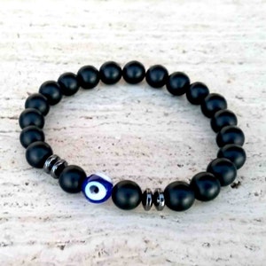 May include: Black beaded bracelet with a blue evil eye charm. The bracelet is made of matte black beads and has a silver accent.