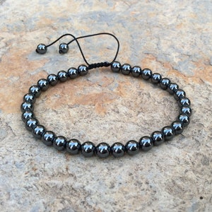 May include: A black beaded bracelet with a black cord closure. The beads are round and have a shiny finish.