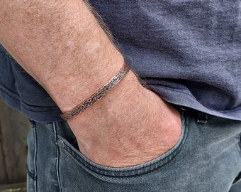 May include: A copper bracelet with a textured design. The bracelet is worn on a person's wrist.