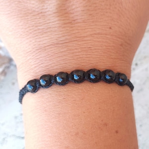 Puede incluir: Pulsera de cuentas negras con siete cuentas redondas y brillantes ensartadas en un cordón oscuro. La pulsera tiene un diseño sencillo y minimalista, adecuado para el uso diario. Las cuentas tienen aproximadamente 1,3 cm de diámetro.
