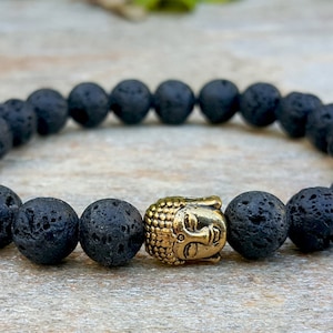 Puede incluir: Pulsera de cuentas de roca volcánica negra con un dije de cabeza de Buda dorado.
