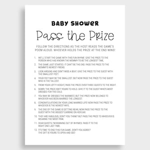 May include: A white paper sign with black text that reads "Baby Shower Pass the Prize." The sign includes instructions for a baby shower game. The text is in a playful, handwritten style.