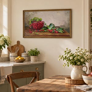 May include: A rectangular framed oil painting depicting a still life of a glass bowl filled with bright red raspberries and green leaves resting on a dark wooden table against a neutral gray background, displayed on a light-colored kitchen wall.