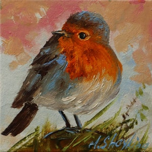May include: An oil painting on canvas depicting a European robin with a vibrant orange-red breast, brown wings, and a grey head. The bird stands amidst green grass against a soft, textured background of muted pink and light blue brushstrokes.