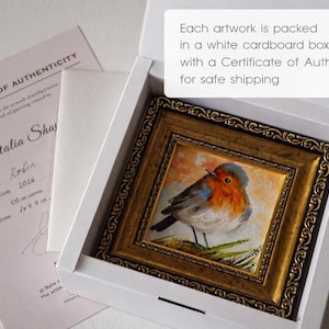 May include: A small oil painting of a robin in an ornate gold frame, nestled inside a white cardboard box. Beside the box lies a Certificate of Authenticity document. The text on the box reads: Each artwork is packed in a white cardboard box with a Certificate of Authenticity for safe shipping.