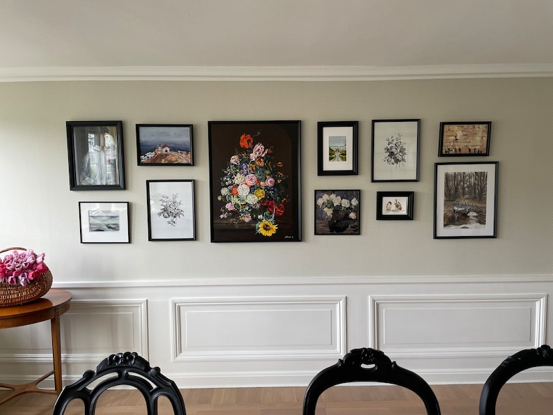 May include: A gallery wall featuring framed art prints of various sizes and styles. The collection includes landscape paintings, floral arrangements, and abstract images, all in black frames. The arrangement is displayed on a neutral-colored wall.