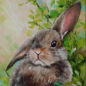 May include: An oil painting on canvas depicting a brown rabbit with one upright ear and one folded ear, positioned amidst vibrant green foliage. The rabbit has dark eyes and a pink nose, with visible brushstrokes and a signature in the bottom corner.