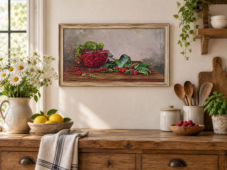 May include: A rectangular framed oil painting depicting a glass bowl filled with bright red raspberries and green leaves resting on a dark wooden surface. The artwork features a neutral gray background and is displayed in a light-colored wooden frame.