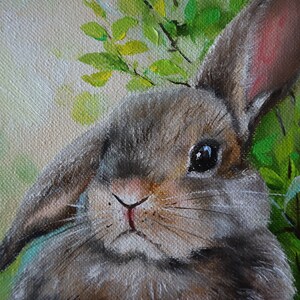 May include: An oil painting on canvas depicting a brown rabbit with one upright ear and one folded ear. The rabbit is positioned against a backdrop of vibrant green leaves and soft, light-colored foliage, rendered with visible brushstrokes.