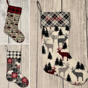 May include: Three Christmas stockings with different patterns. The first stocking has a red and black plaid cuff and a white background with brown bears, deer, and trees. The second stocking has a red and black plaid cuff with a white background and a black and white plaid pattern. The third stocking has a red and black plaid cuff with a white background and a black and white plaid pattern with a red and black plaid deer.