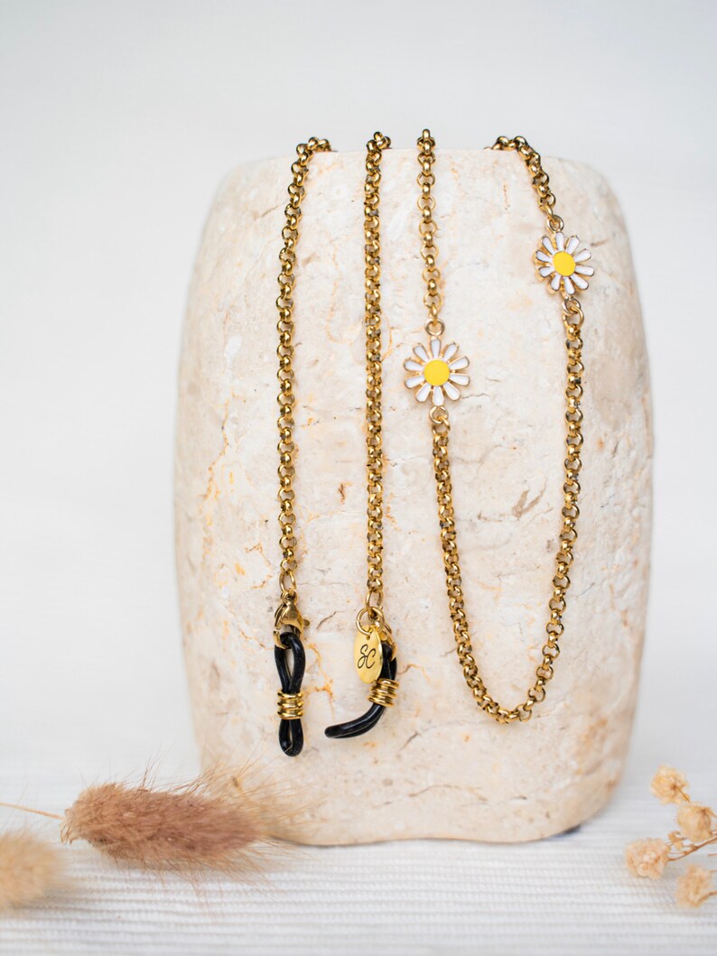 May include: Two gold chain glasses retainers with black rubber ends and small white and yellow daisy charms.