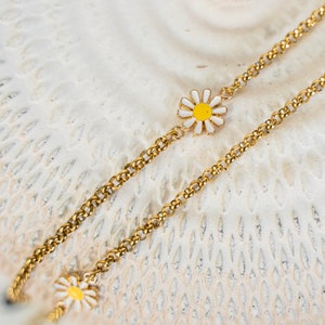 May include: A gold chain necklace with two small white and yellow daisy charms.