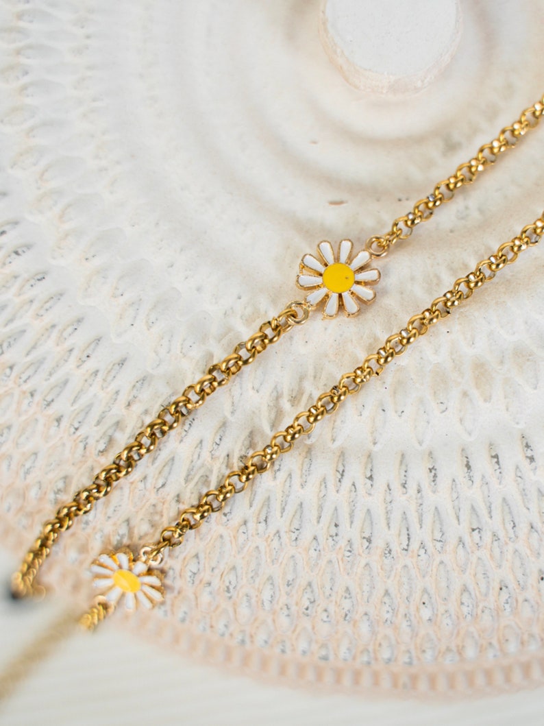 May include: A gold chain necklace with two small white and yellow daisy charms.