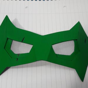 May include: A bright green mask with angular edges and eye openings. The eye openings are filled with a white mesh material. The mask is made of a solid material and is likely for costume or cosplay purposes.