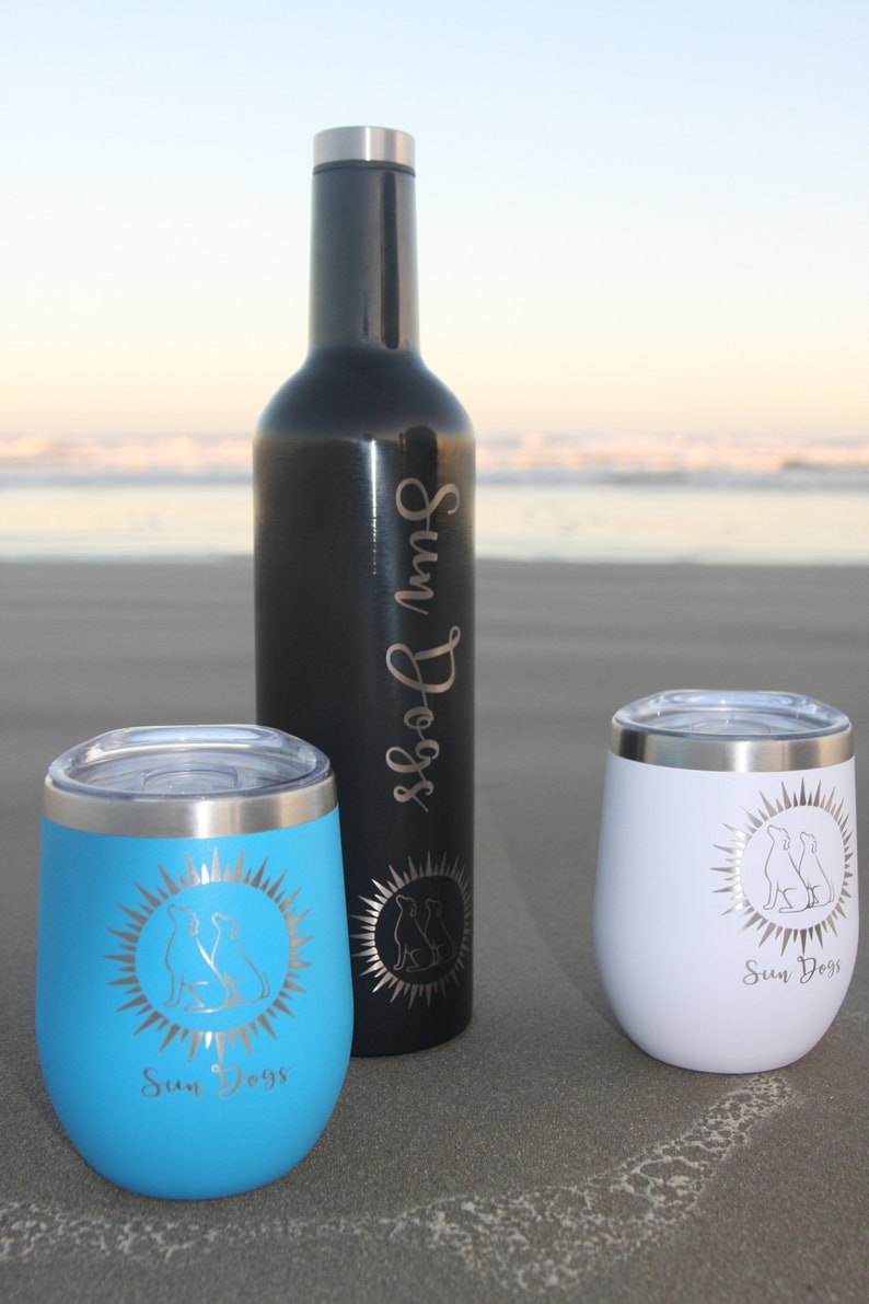 May include: Three stainless steel tumblers with a sun and two dogs design. The tumblers are in blue, white, and black. The black tumbler is a bottle.
