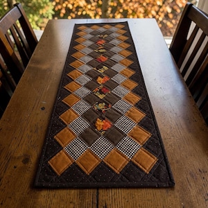 May include: A rectangular quilted table runner featuring a diamond-patterned patchwork design. The fabric squares alternate between solid brown, solid mustard yellow, black and white gingham, and a central row of autumn leaf prints.
