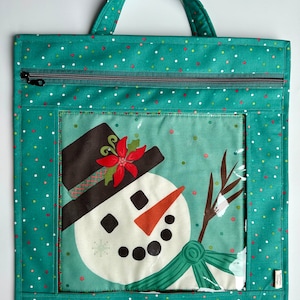 May include: Teal zippered tote bag with a clear window featuring a snowman with a red poinsettia on his hat. The bag has a white polka dot pattern.