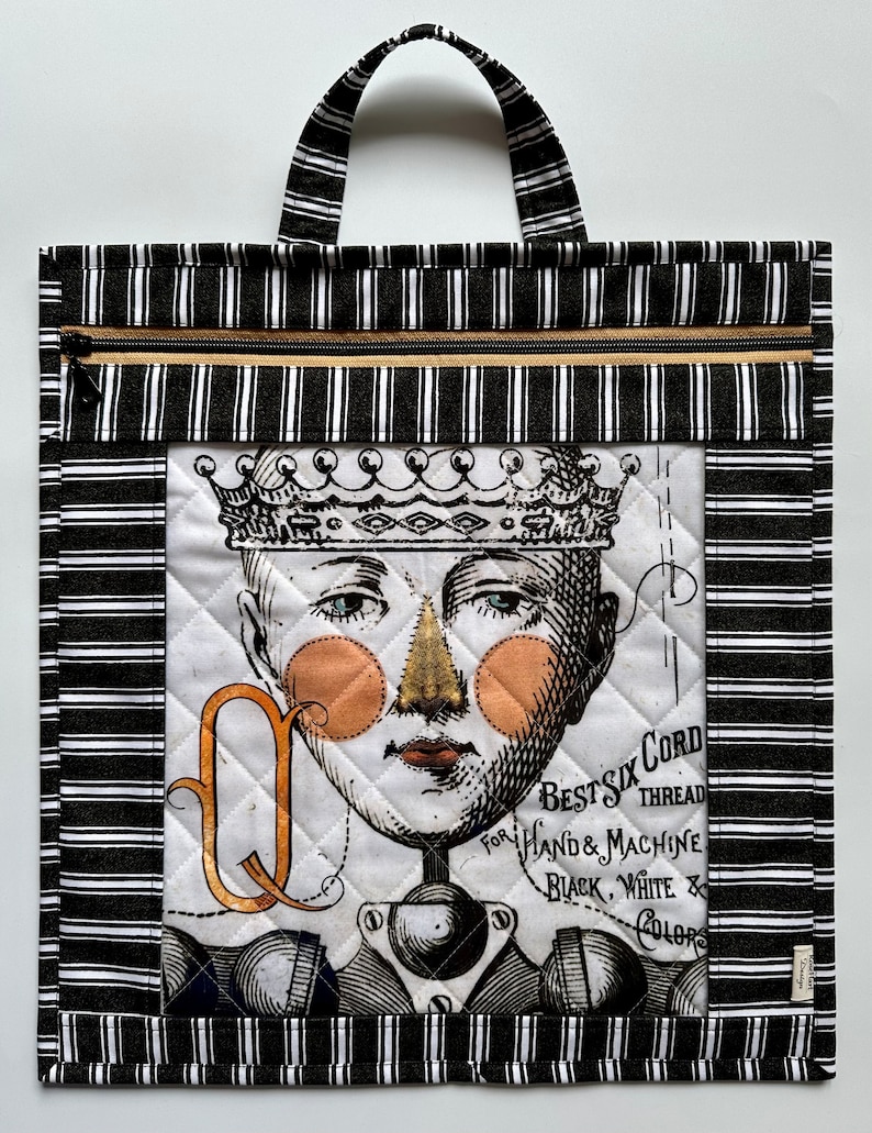 May include: Black and white striped tote bag with a zipper closure. The front of the bag features a quilted panel with a vintage illustration of a person wearing a crown and a gold letter Q. The illustration includes the text "Best Six Cord for Hand & Machine Thread Black, White & Colors".