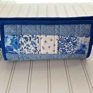 May include: A blue quilted fabric bag with a rectangular shape and two handles. The bag features a patchwork design with various blue floral patterns and solid blue accents. The bag is approximately 12 inches long.