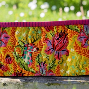 May include: A rectangular quilted fabric pouch featuring a vibrant yellow background with a repeating pattern of stylized deer, large pink and purple flowers, and green foliage. The pouch has two side handles and trim in a dark pink striped fabric.