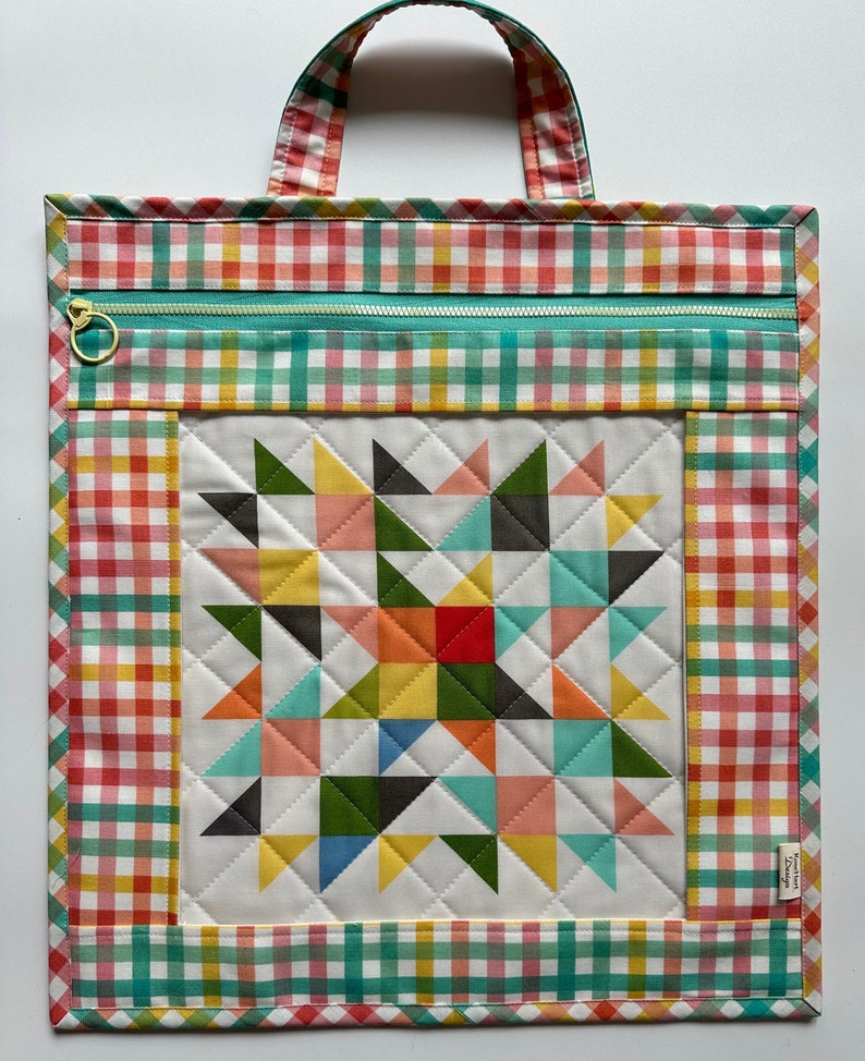 May include: A quilted tote bag with a gingham pattern in shades of red, yellow, and green. The bag has a zipper closure and a patchwork design with a star in the center. The bag has a label that says "Sweetheart Designs".