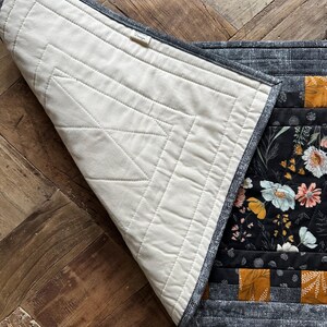 Puede incluir: Un camino de mesa de tela floral en blanco y negro con un patr&oacute;n geom&eacute;trico amarillo mostaza. El camino de mesa est&aacute; acolchado y tiene un respaldo de algod&oacute;n blanco. El camino de mesa est&aacute; doblado por la mitad y el respaldo es visible.