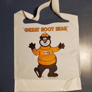 May include: White plastic shopping bag with a brown bear wearing a yellow sweater with the letters "A&W" on it. The bag has the text "Great Root Bear" in black letters.