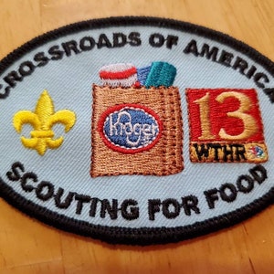 May include: A blue and white oval-shaped patch with the text "Crossroads of America Scouting for Food" and a yellow fleur-de-lis. The patch also features a brown paper bag with a red and white grocery item, a blue circle with the word "Kroger" and a red square with the number "13" and the text "WTHR".