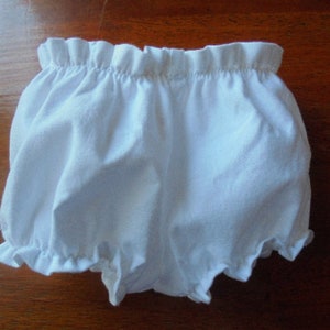 May include: White baby bloomers with a ruffled elastic waistband and leg openings. The bloomers are made of a soft, lightweight fabric, perfect for warm weather. The garment is designed for comfort and ease of movement.