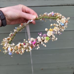 以下が含まれることがあります： 白、ピンク、青、緑の乾燥花でできた繊細な花冠。白いリボンで結ばれています。