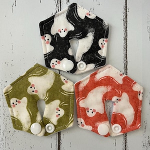 May include: Three hexagonal fabric pads with a ghost pattern. One pad is black and white, another is green and white, and the third is orange and white. Each pad has a white snap closure.
