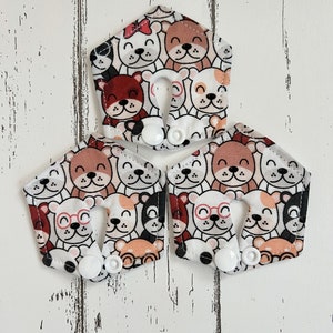 May include: Three white fabric bibs with a pattern of cartoon animals with different expressions. The bibs have white snaps on the sides.