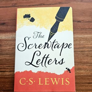 May include: A hardcover book titled "The Screwtape Letters" by C.S. Lewis. The cover features a black pen nib, black ink splotches, and a red and yellow color scheme. The title is in elegant script.