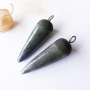 Peut inclure: Deux pendentifs en céramique bleu foncé en forme de larme avec des boucles en fil d'argent. Les pendentifs ont une surface marbrée et texturée.