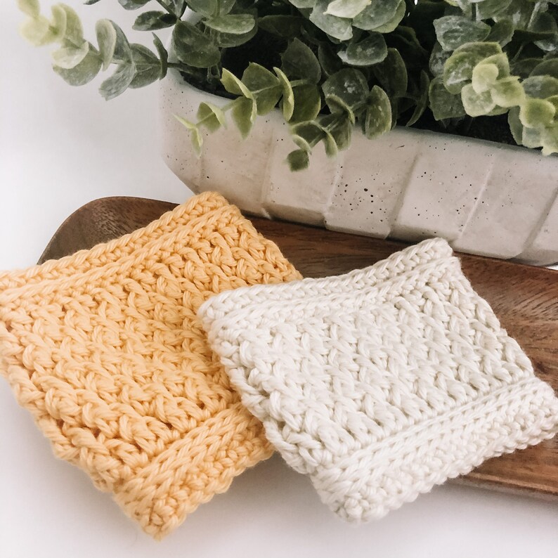 May include: Two crocheted dishcloths, one yellow and one white, on a wooden surface.