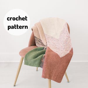 May include: A crocheted throw blanket in shades of green, pink and beige, draped over a chair. The blanket features a chevron pattern.